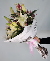 A hand-tied lily bouquet in natural paper with pink ribbon; reference of lily presentation. Photo: rehman yousaf / Pexels. Reference image; final flowers and wrap subject to florist confirmation.