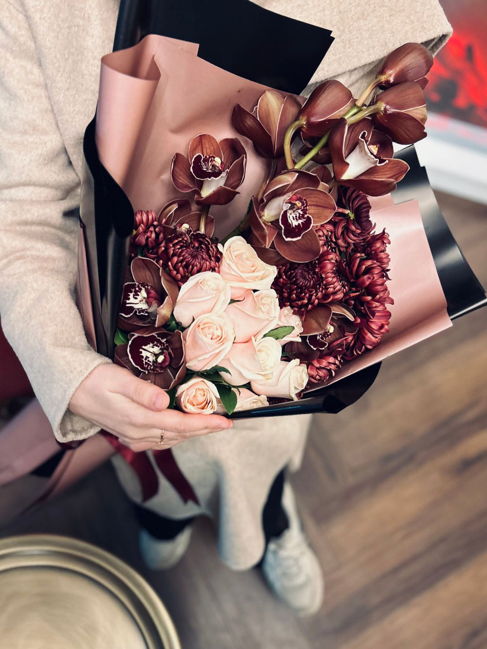 A hand-tied orchid and rose bouquet held in a neutral-toned interior; reference image for proposed arrangement. Photo: Ssümçiğ / Pexels. Reference image; final flowers and wrap subject to florist confirmation.