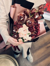 A hand-tied orchid and rose bouquet held in a neutral-toned interior; reference image for proposed arrangement. Photo: Ssümçiğ / Pexels. Reference image; final flowers and wrap subject to florist confirmation.