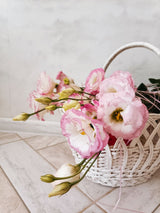 Pink lisianthus in a white woven flower basket against a pale backdrop; example of a florist's-choice basket, actual contents vary. Photo: elena_sher / Pexels.