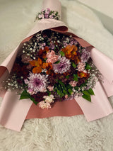 Mixed seasonal flowers in soft pink wrapping, illustrative arrangement.