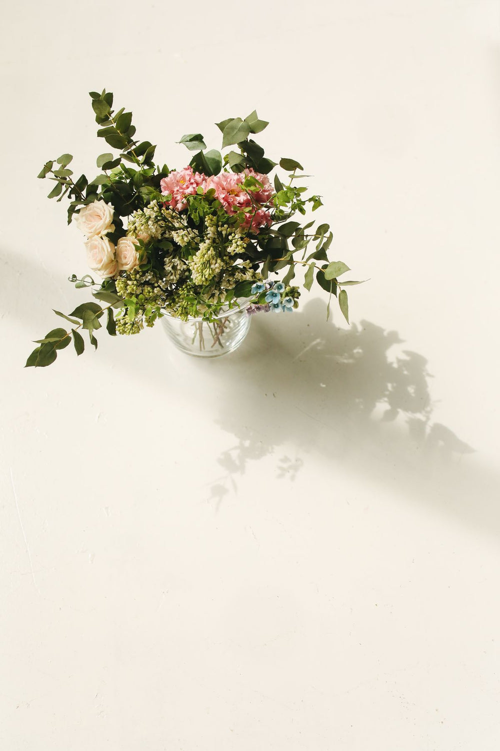 Fresh seasonal flowers in a clear vase on a white background; home-flower arrangement styling example. Photo: Polina Tankilevitch / Pexels.